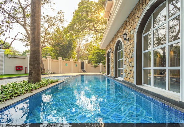 A swimming pool with clear blue water, surrounded by stone walls and large windows. - Enrise by Sayaji Lonavala (Mawal)