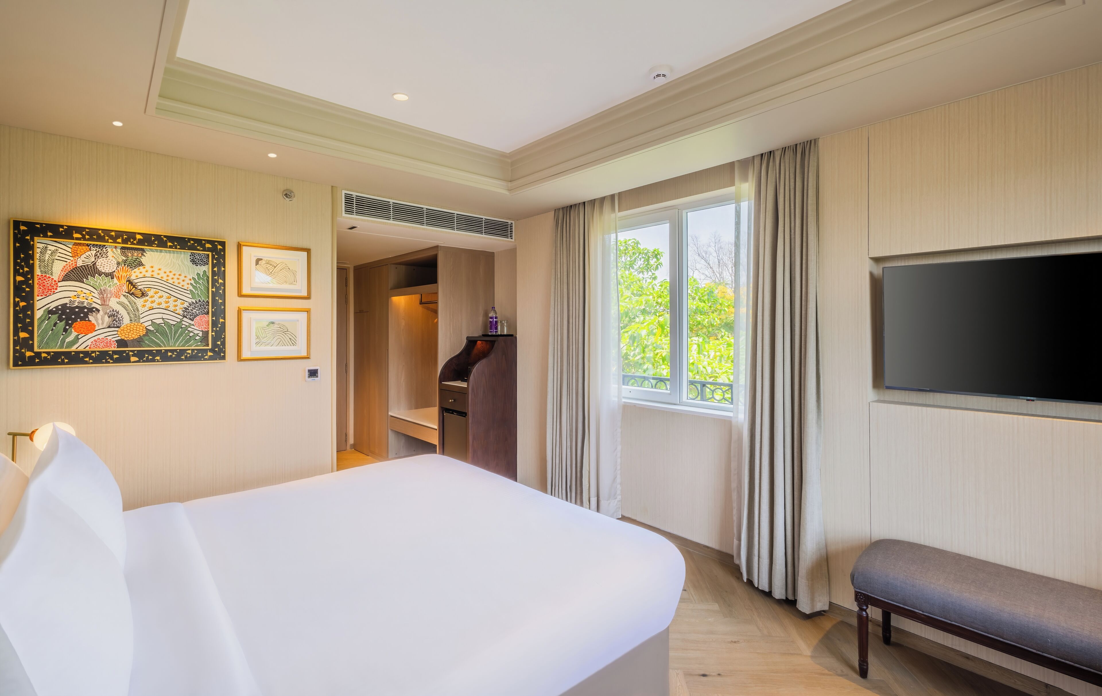 Een hotelkamer met een groot bed, een flatscreen televisie, een bankje en kunst aan de muur.