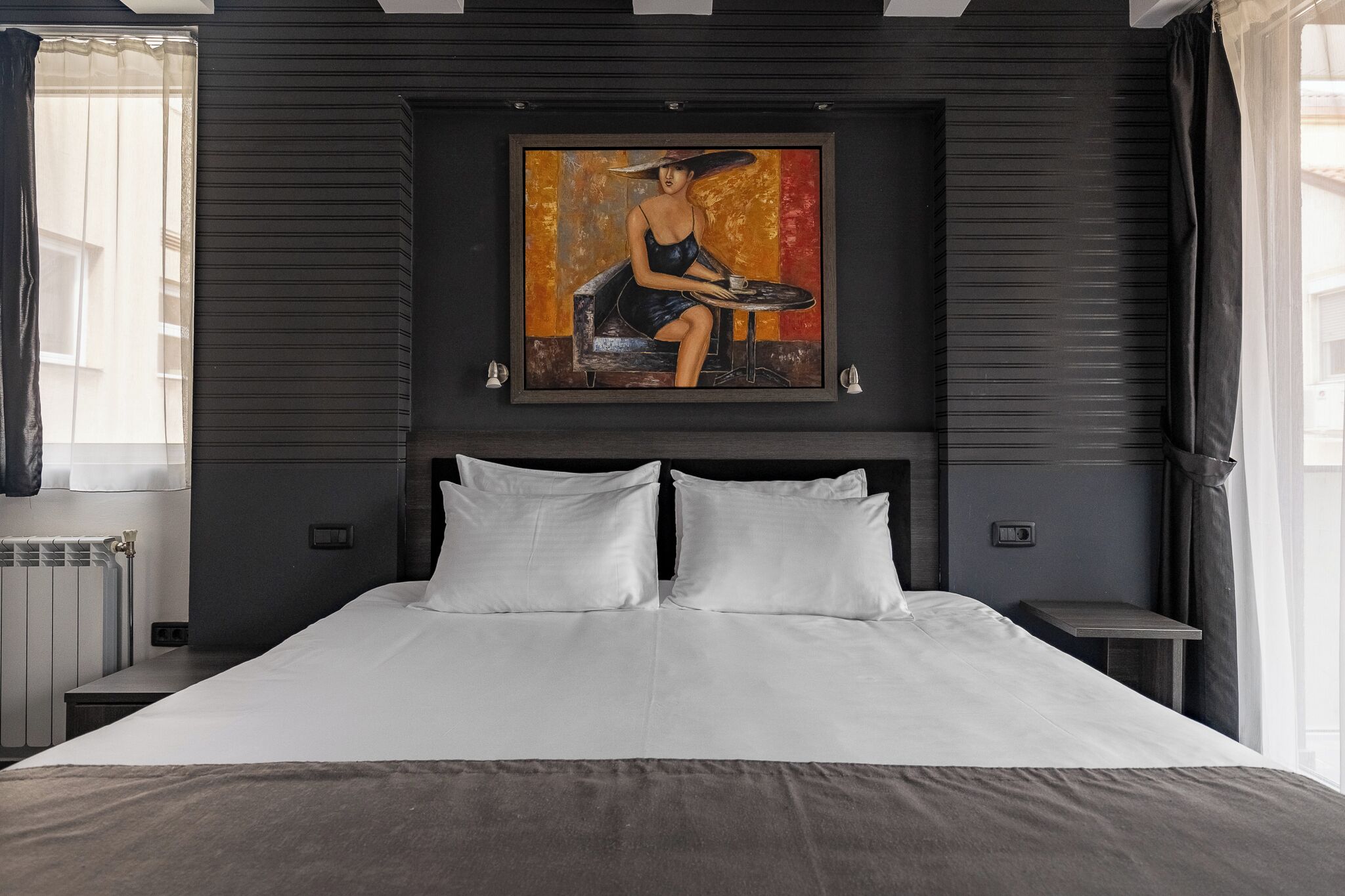 A modern hotel room with a large bed, a painting on the wall, and a window with curtains.