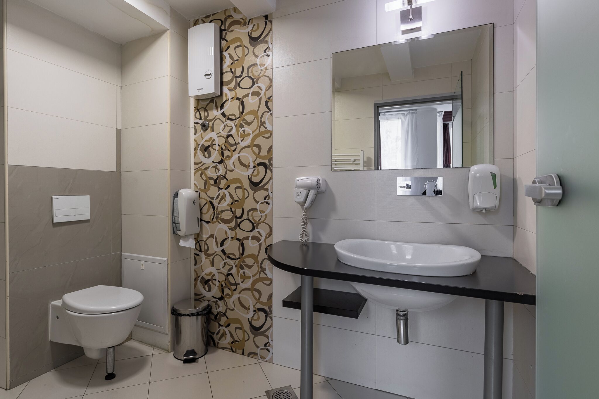 Een badkamer met toilet, wastafel, spiegel en een behang met een patroon.