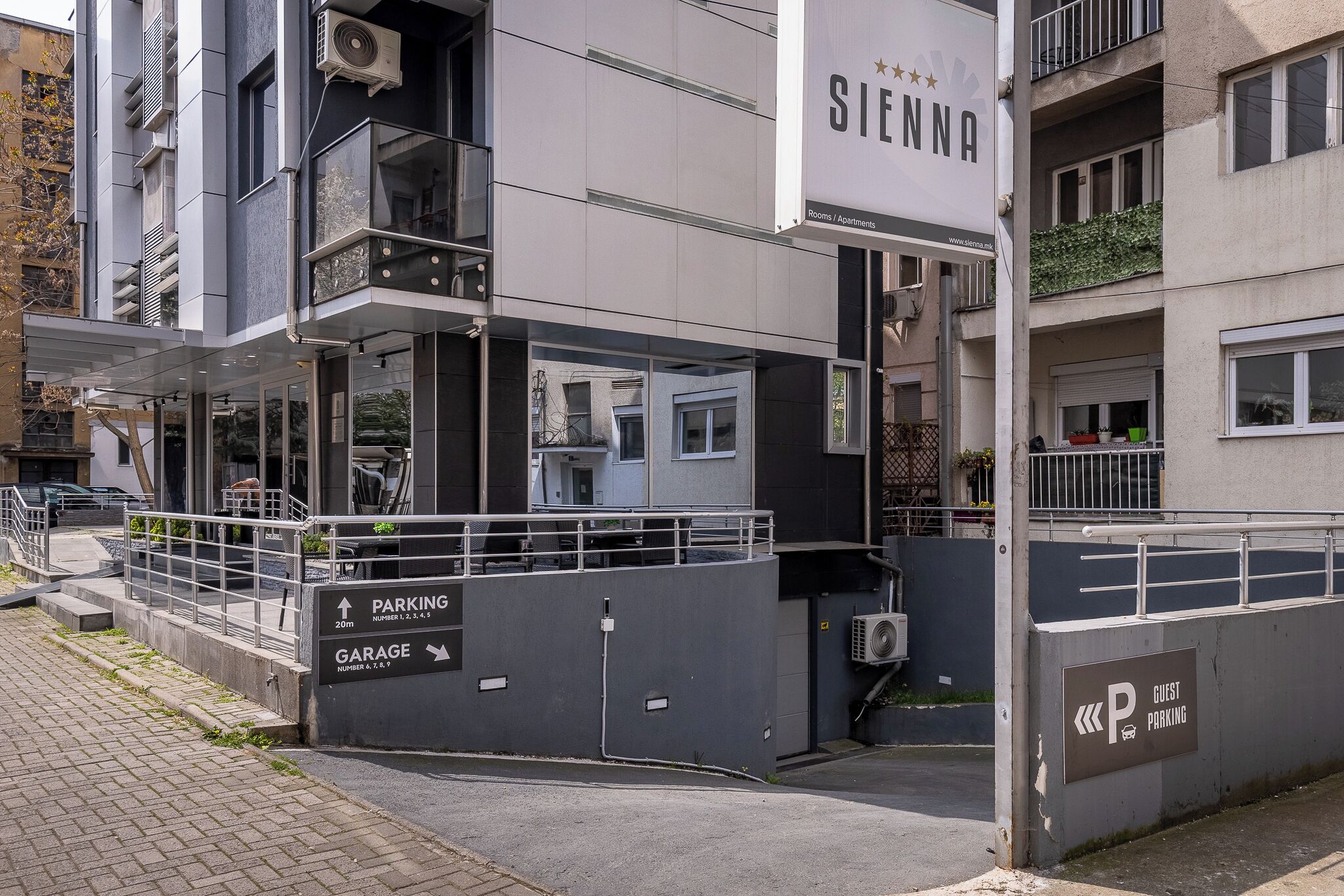 A modern building with a sign for 'Sienna' indicating it is a hotel. There are signs for 'PARKING' and 'GARAGE' with numbers.