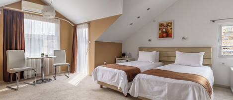 A hotel room with two beds, a desk with chairs, a small table, and a window with curtains.