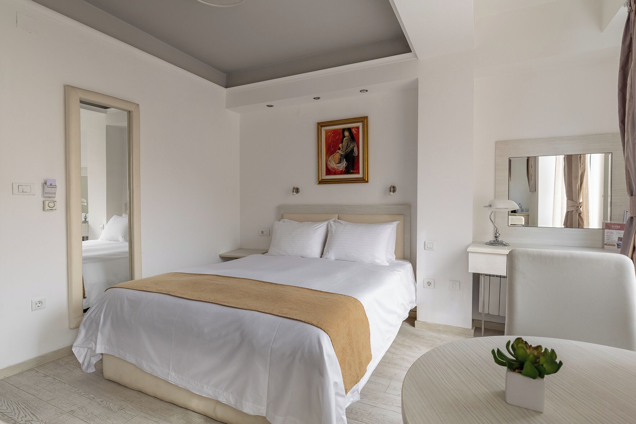 A hotel room with a bed, bedside table, chair, and a small table with a plant.