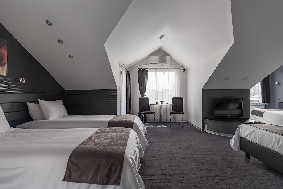 Een hotelkamer met twee bedden, een televisie, een klein tafeltje met stoelen en een plafondventilator.
