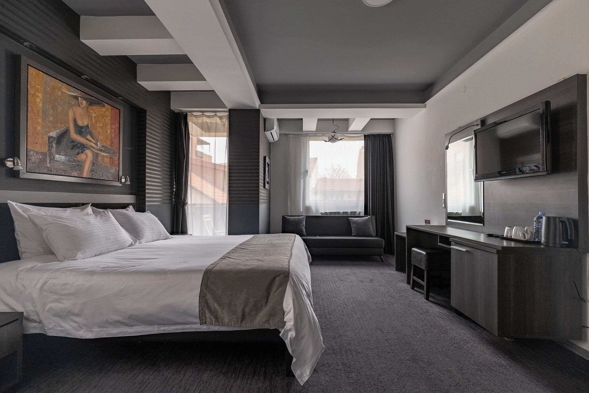 A modern hotel room with a large bed, a sofa, a desk, and a television.