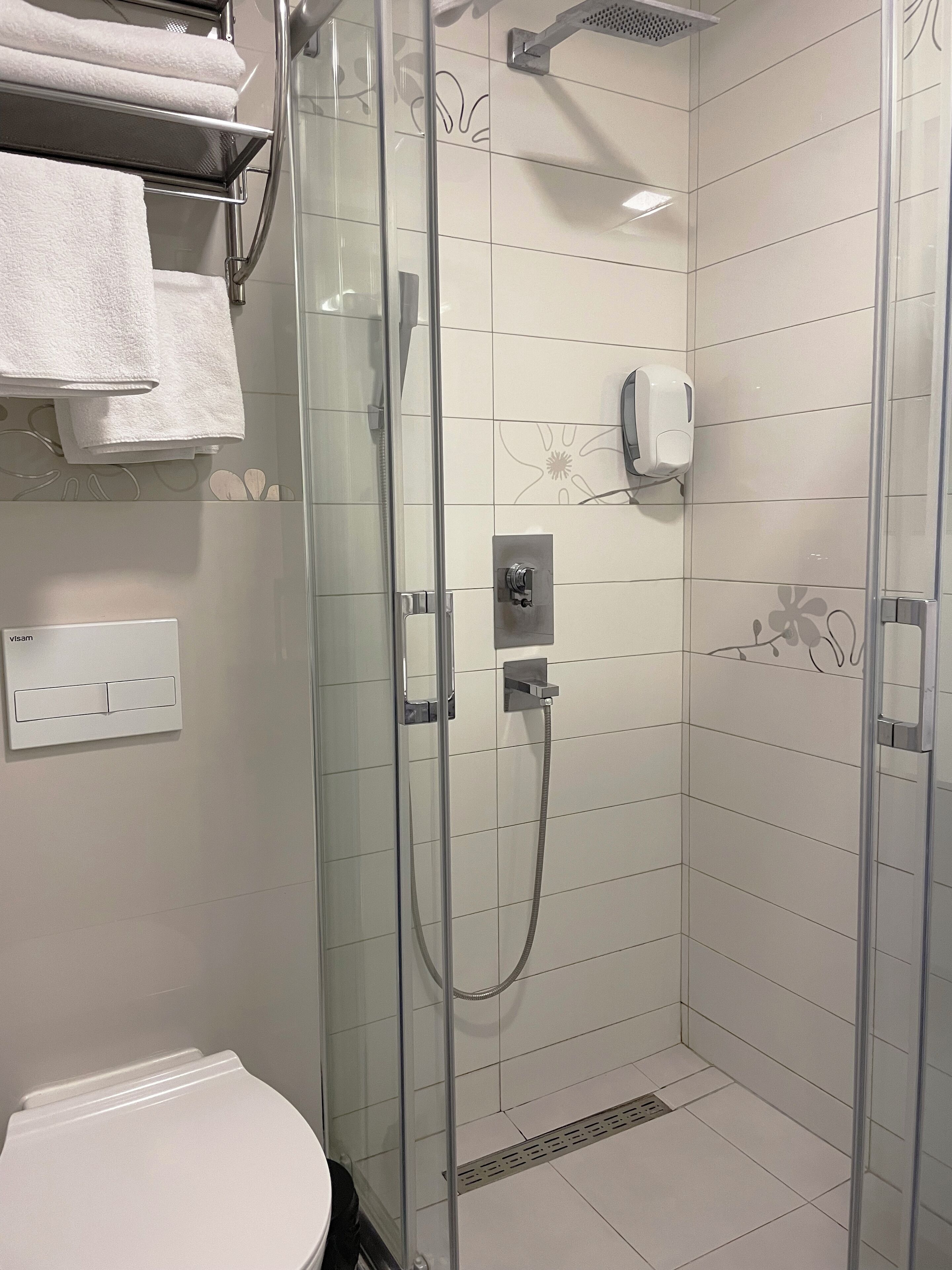 Una doccia moderna con porta in vetro, soffione a mano e dispenser di sapone a parete.