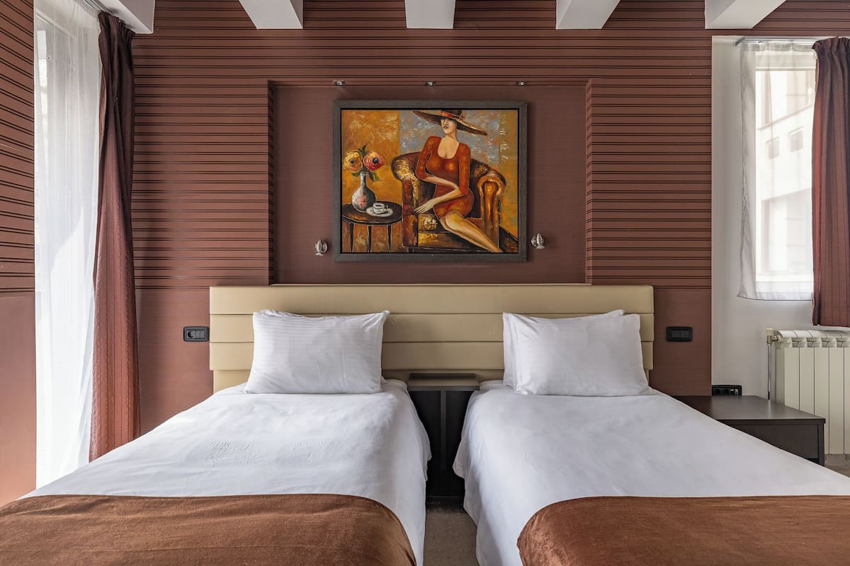 Hotelkamer met twee bedden, een schilderij aan de muur, een klein tafeltje met een vaas en een raam met gordijnen.