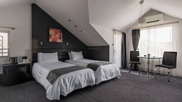 A hotel room with two beds, a desk, a chair, a small table, and an air conditioning unit.