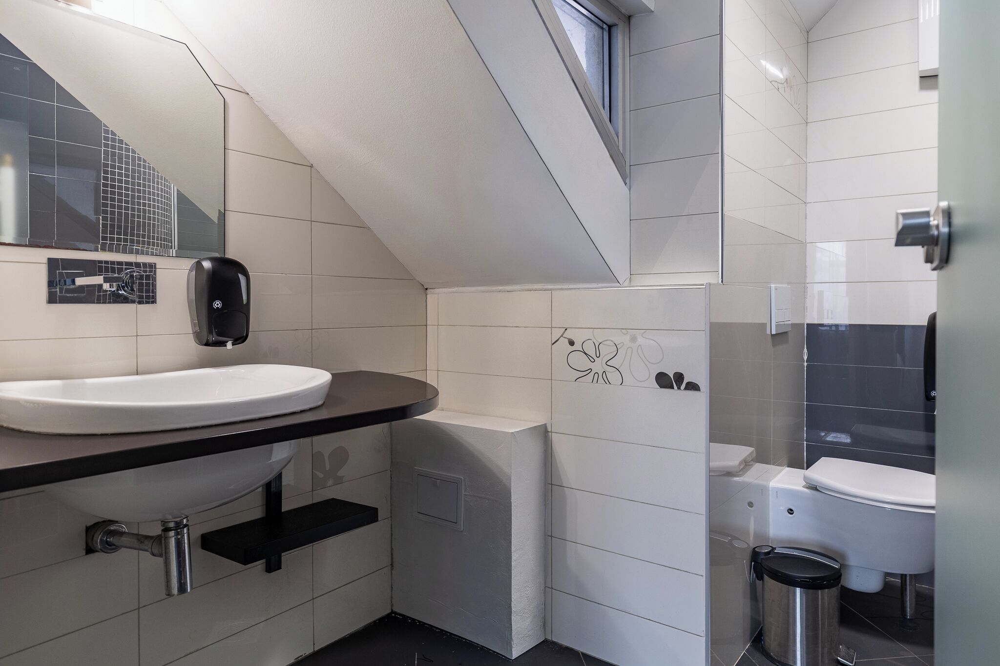 A modern bathroom with a white sink, black countertop, and a glass shower enclosure.