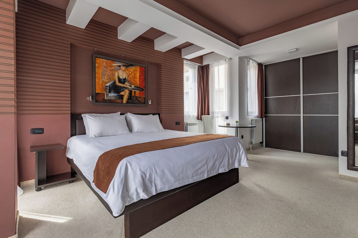 Een moderne hotelkamer met een groot bed, een schilderij erboven, een bureau en een kledingkast.