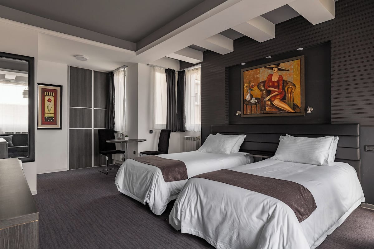 Een moderne hotelkamer met twee bedden, een bureau, een stoel en een schilderij aan de muur.