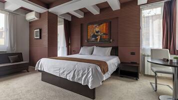 A bedroom with a bed, a sofa, a table, a painting, and a radiator.