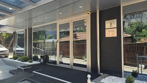 Una entrada de hotel moderna con puertas de vidrio, una escalera de metal y un cartel que indica el horario de atención.