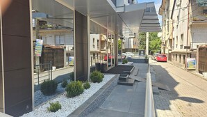 Un edificio moderno con fachada de vidrio, un acceso cubierto y un camino pavimentado con guijarros blancos y pequeños arbustos.