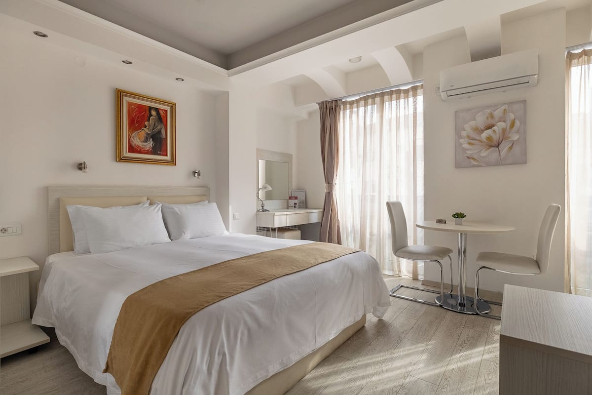 Hotelkamer met een bed, een bureau, een stoel, een tafeltje en een raam met gordijnen.