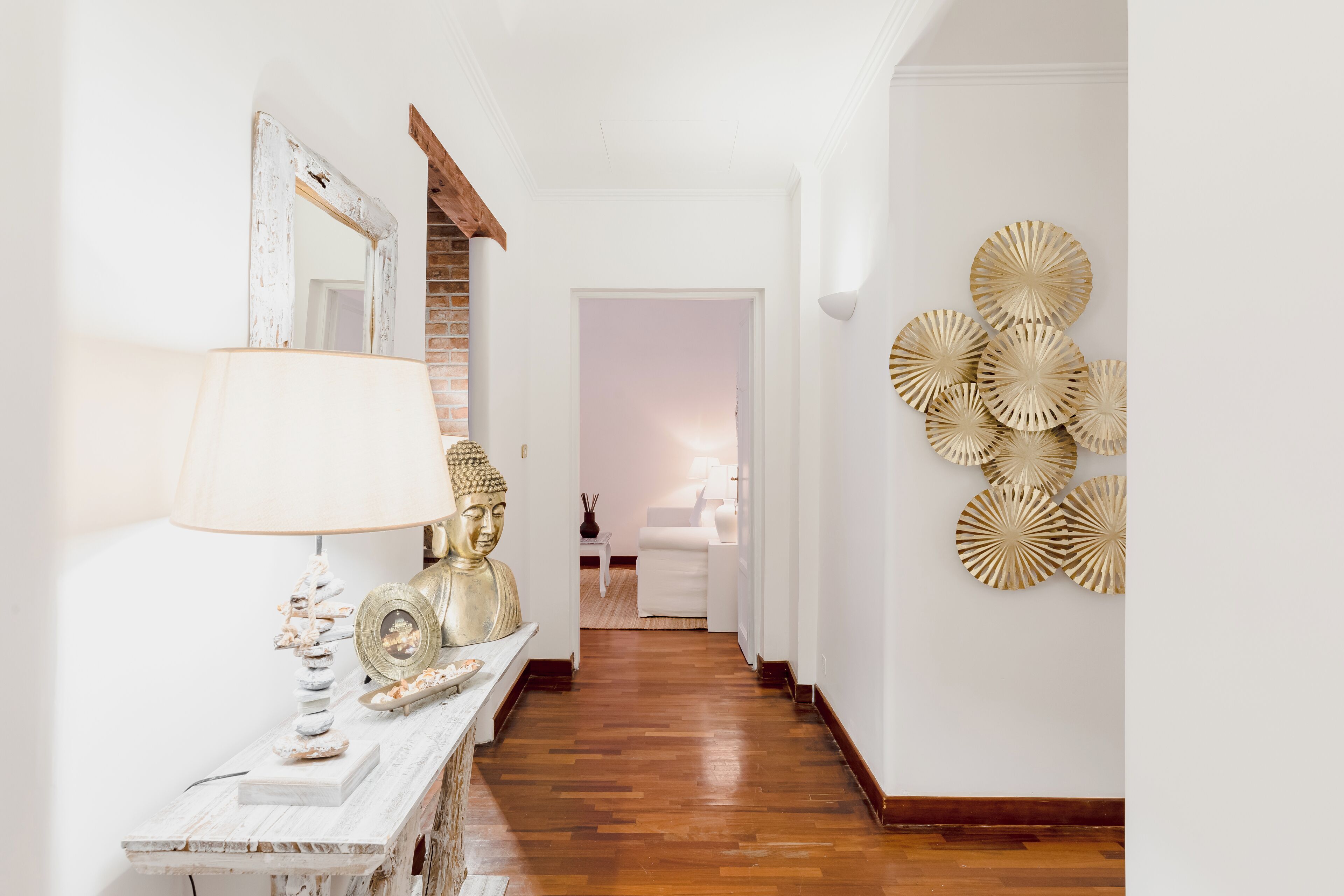 A hallway with a wooden floor, a white wall with decorative plates, and a mirror with a rustic frame.