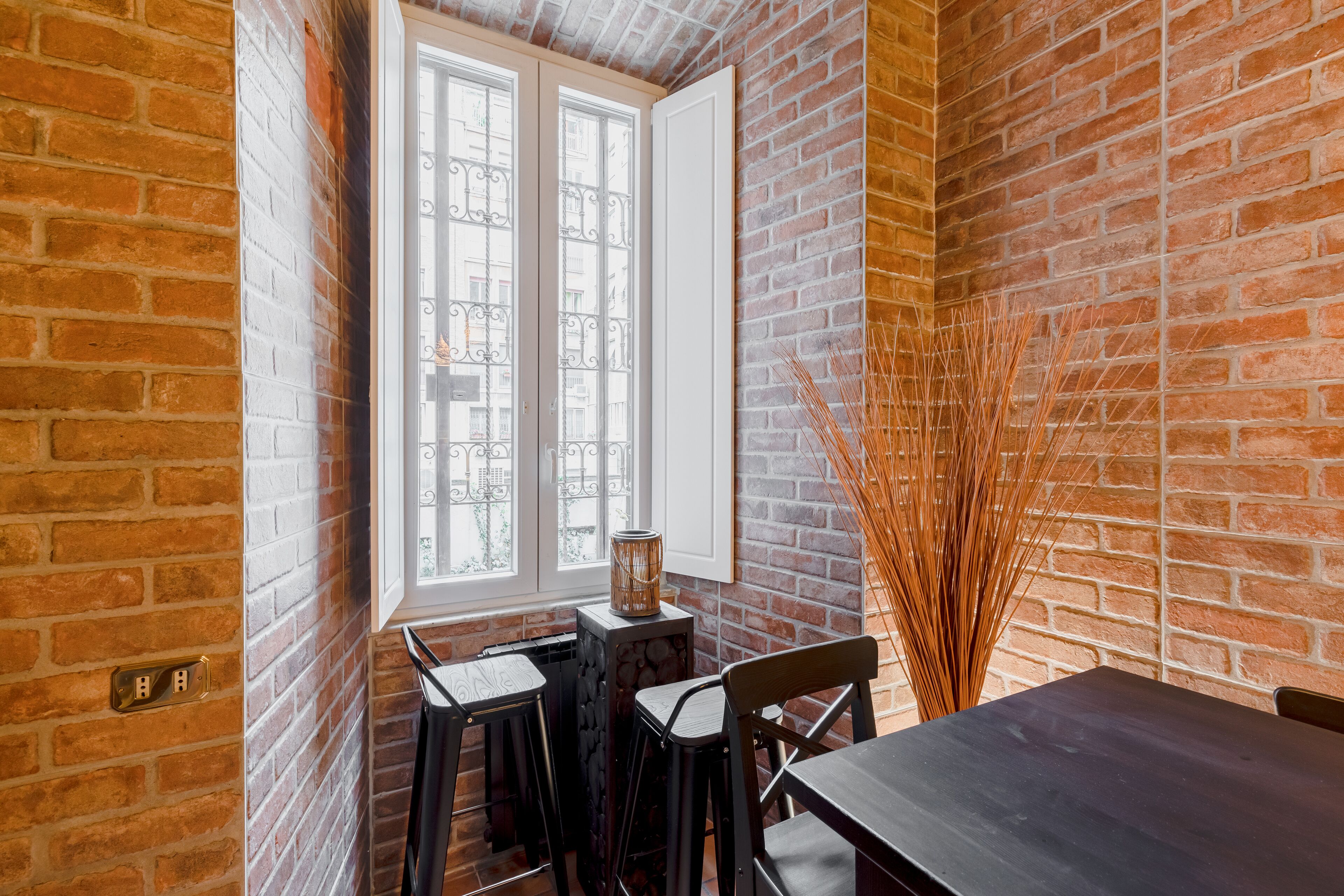 A dining area with a brick wall, a window with metal bars, a table, and chairs.