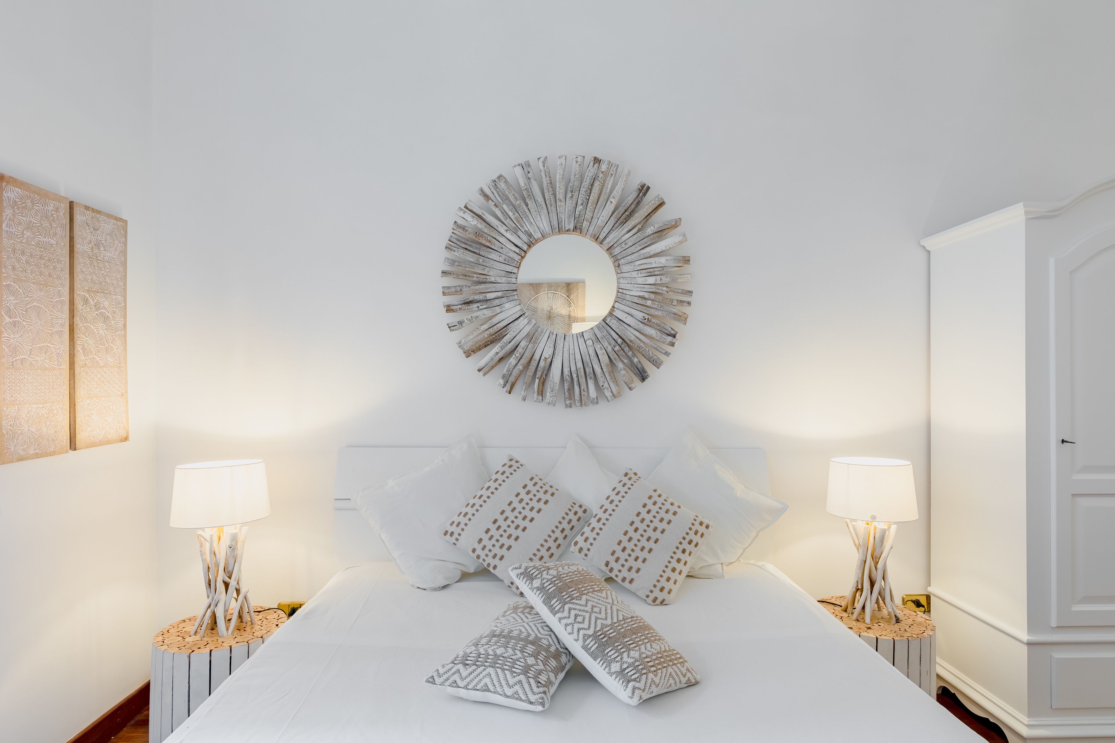 A neatly arranged bedroom with a bed, two bedside tables, a wall-mounted mirror, and a wardrobe.