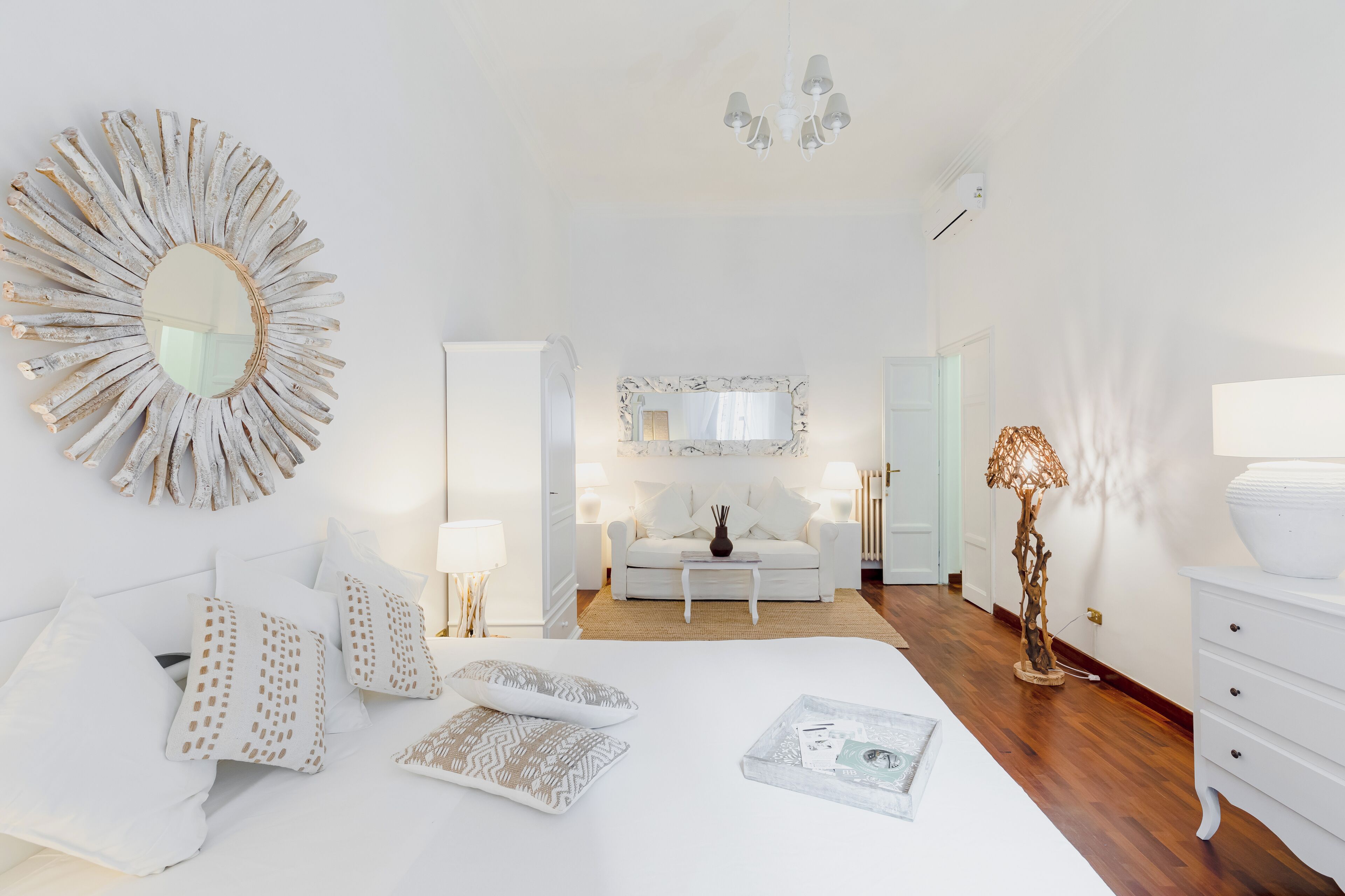 A bright, white bedroom with a large mirror, a white sofa, and a wooden floor.