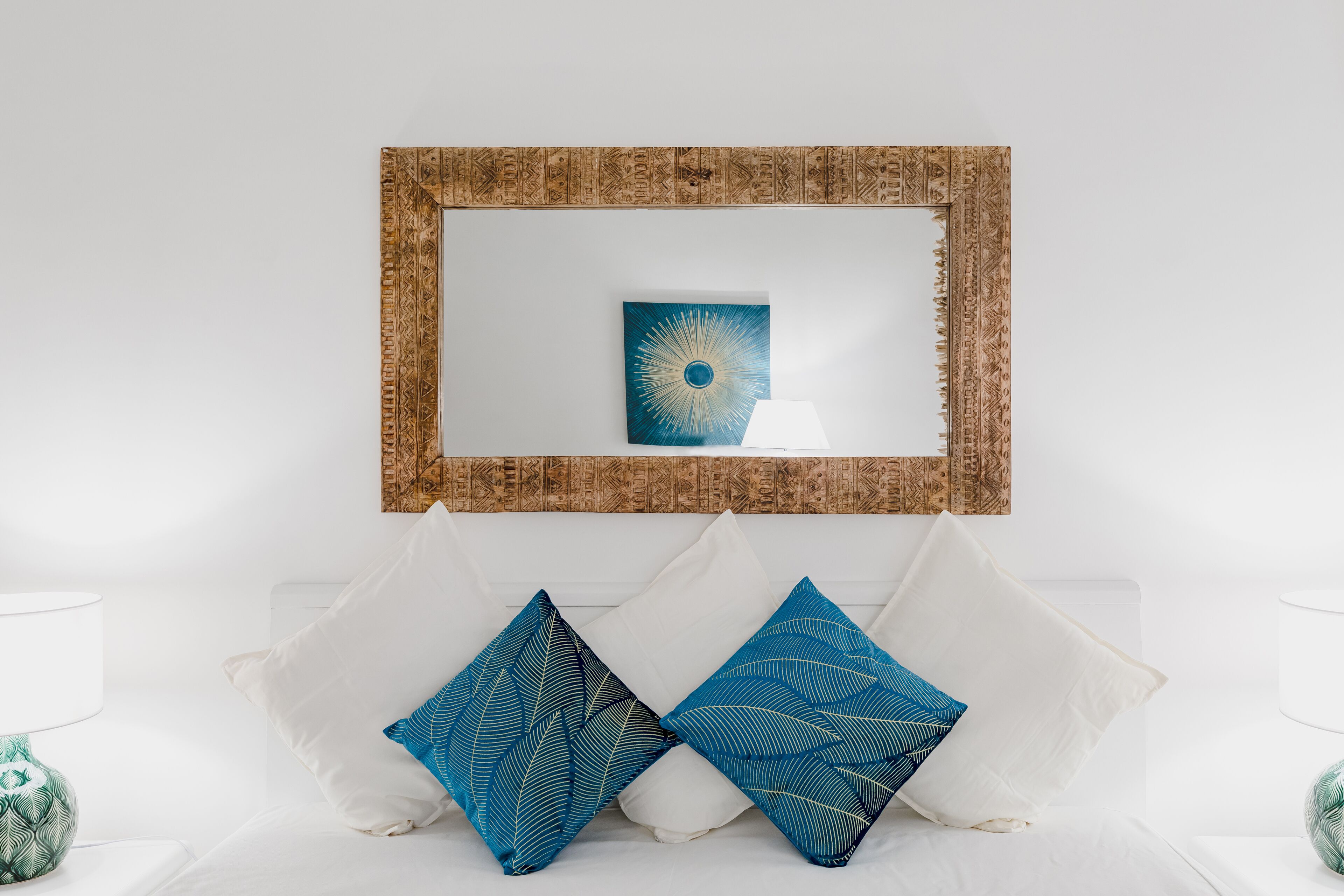 Un canapé blanc agrémenté de deux coussins bleus à motifs, et une œuvre d’art encadrée est accrochée au-dessus.