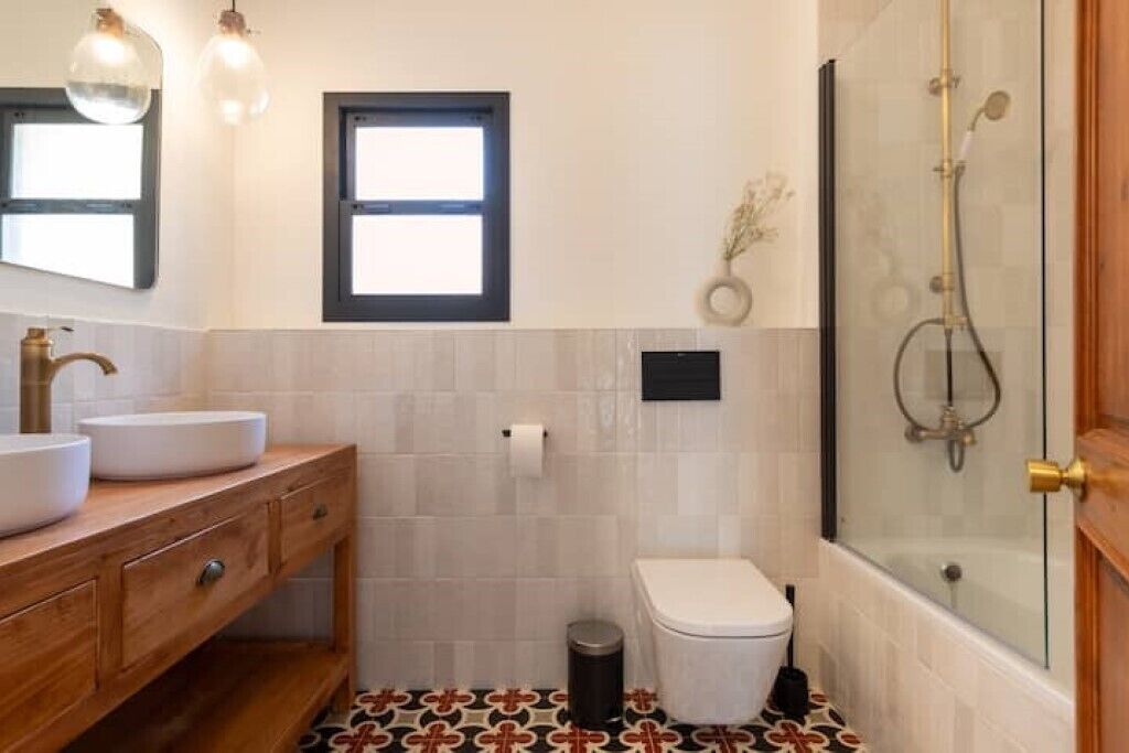 Ein Badezimmer mit einem Holz-Waschtisch, einer Toilette, einer Duschkabine und einem gemusterten Boden.