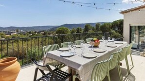 Une table à manger installée à l’extérieur, avec des chaises, donnant sur la campagne, et un pot placé sur la table.