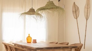 Un coin repas avec une table en bois, des chaises en osier et des lampes vertes suspendues.