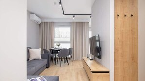 Una sala de estar moderna con un sofá gris, un mueble de televisión de madera y un comedor con mesa y sillas.