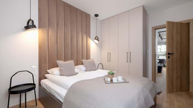 Un dormitorio moderno con una cama grande, un armario de madera y una mesita con tazas.