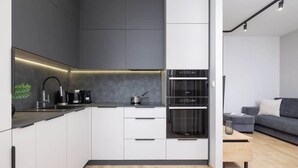 Una cocina moderna con gabinetes blancos, encimera negra y electrodomésticos de acero inoxidable.
