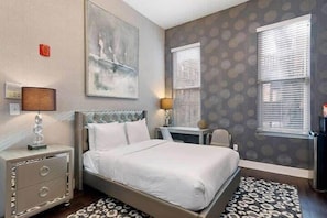 A bedroom with a large bed, a nightstand, a desk, and a chair.