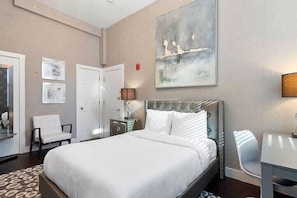 A hotel room with a large bed, a bedside table with a lamp, a chair, and a painting on the wall.