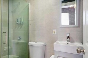 Un baño con cabina de ducha de vidrio, inodoro y lavamanos con espejo superior.
