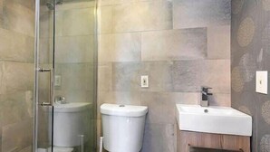 A bathroom with a glass shower enclosure, a toilet, and a sink with a wooden cabinet. - Bay VIllage Suite, Ready To Host! (Boston)