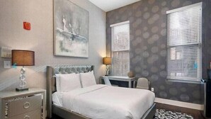 Habitación de hotel con cama, mesita de noche, lámpara y una obra de arte en la pared.