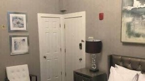 Una habitación de hotel con una cama, una silla, una mesita de noche, una lámpara y una puerta.