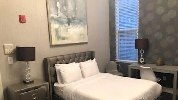 Quarto com cama, mesa de cabeceira, escrivaninha e janela com persianas.