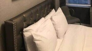 Quarto com cabeceira, cama com roupa de cama branca, janela com persianas e um quadro na parede.