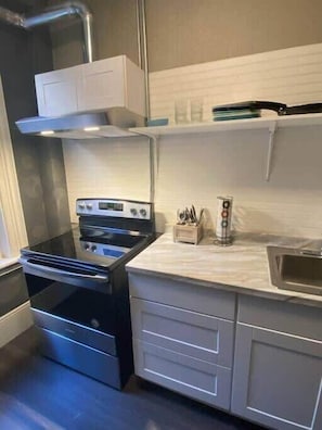 A compact kitchen with a built-in stove, a microwave, and a stainless steel range hood. There are white cabinets and a countertop with a knife block and a small sink.