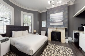 A bedroom with a large bed, a fireplace, and a modern kitchen area.