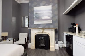 A hotel room with a fireplace, a bed, a chair, a desk with a lamp, a microwave, and a dishwasher. - Private Studio In Boston's Bay Village! (Boston)
