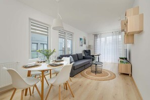 Una sala de estar moderna con comedor, que presenta un sofá gris, sillas blancas, una mesa redonda de centro y piso de madera.