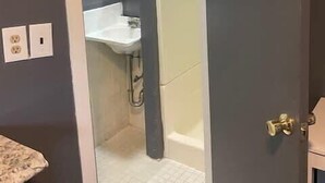 Een badkamer met een wit wastafelmeubel, een badkuip en een deur naar een andere kamer.