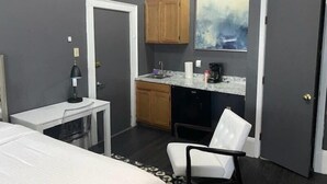 Een compacte hotelkamer met een bed, een bureau met stoel, een kleine kitchenette en een schilderij aan de muur.