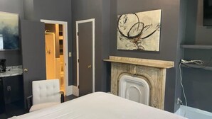 Een slaapkamer met een bed, een witte stoel, een open haard en een schilderij aan de muur.
