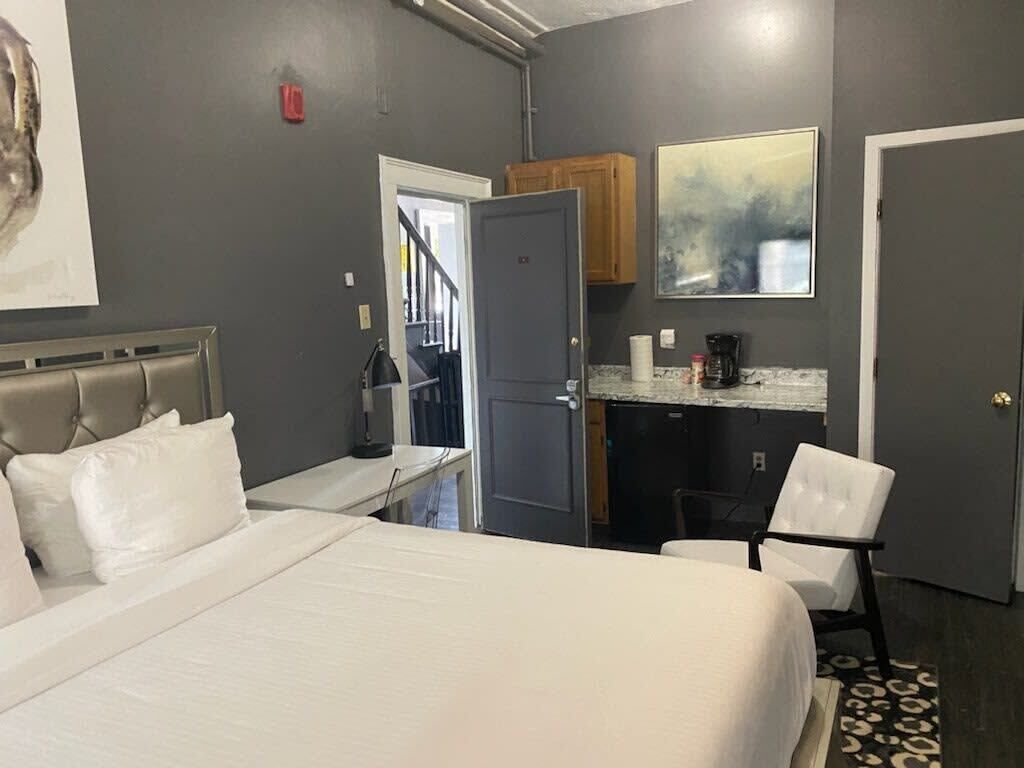 Une chambre d’hôtel comprenant un lit, un bureau, une chaise, une kitchenette et une porte donnant sur une autre pièce.