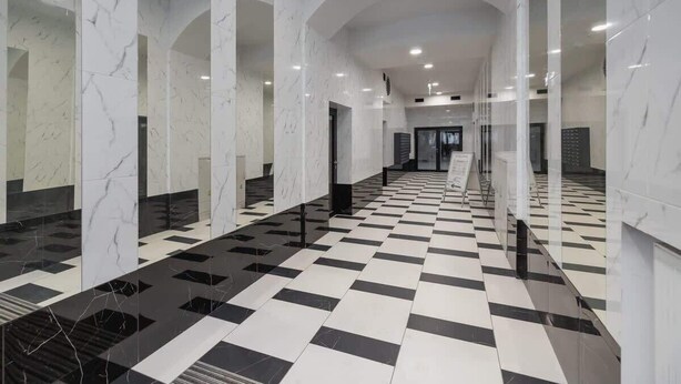 Un couloir aux murs de marbre blanc et au sol carrelé de motifs noirs et blancs.