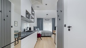 A modern, compact hotel room with a kitchenette, a bed with a gray headboard, and a large window with curtains. - Modern Studio in the Center | Balcony and Workspace (Poznan)
