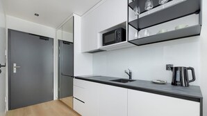 A modern kitchen with white cabinets, a black countertop, a built-in microwave, and a coffee maker. - Modern Studio in the Center | Balcony and Workspace (Poznan)