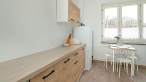 A compact kitchen with a wooden countertop, a white refrigerator, and a dining table with white chairs.